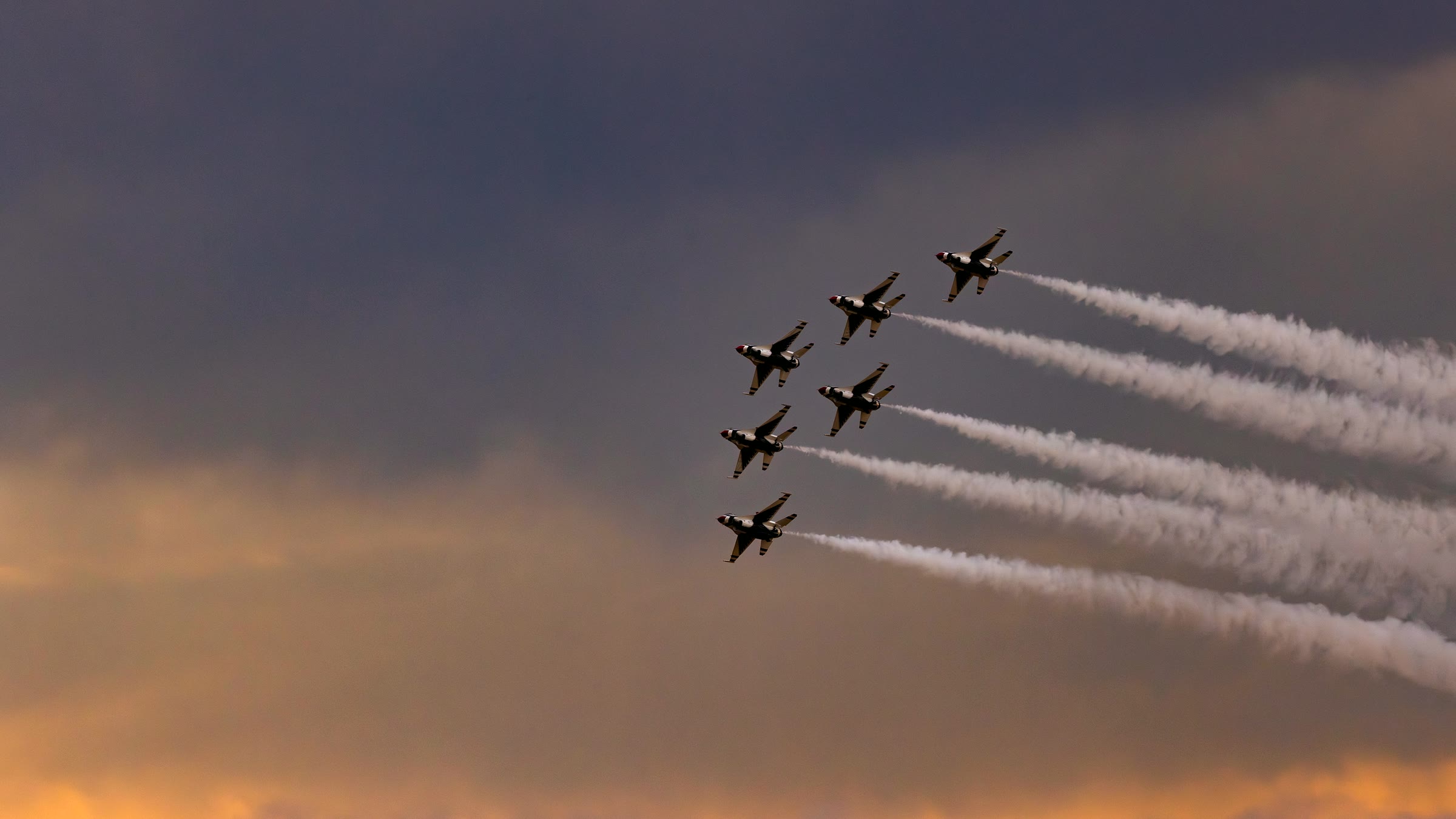 A formation of display aircraft trailing smoke against a golden sky