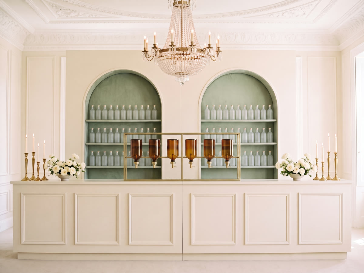 A long panelled scent bar counter before twin arched niches of frosted bottles, amber dispensers centred on a brass rack